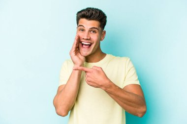 Kafkasyalı genç adam mavi arka planda izole edilmiş. Dedikodu yapıyor, bir şeyleri bildiriyor..