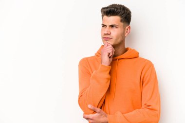 Beyaz arka planda izole edilmiş genç beyaz bir adam şüpheli ve şüpheci bir ifadeyle yana bakıyor..