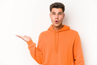 Beyaz arka planda izole edilmiş genç beyaz adam, avuç içi fotokopi alanını elinde tutmaktan etkilenmiş..