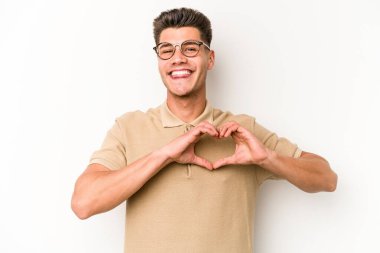 Beyaz arka planda izole edilmiş genç beyaz bir adam gülümsüyor ve elleriyle kalp şekli gösteriyor..