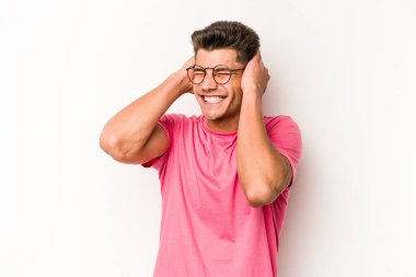 Beyaz arka planda izole edilmiş genç beyaz bir adam kulaklarını elleriyle kapatıyor..