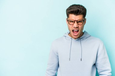 Kafkasyalı genç adam mavi arka planda izole edilmiş. Çok kızgın, öfkeli, hayal kırıklığına uğramış..