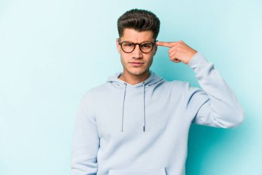 Mavi arka planda izole edilmiş genç beyaz bir adam şakağı parmağıyla işaret ediyor, düşünüyor ve bir göreve odaklanıyor..