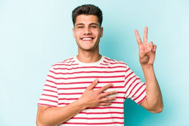 Kafkasyalı genç adam mavi arka planda izole edilmiş yemin ediyor, elini göğsüne koyuyor..