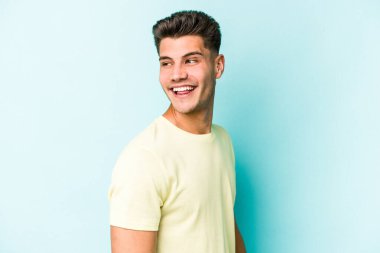 Mavi arka planda soyutlanmış genç beyaz bir adam gülümsüyor, neşeli ve keyifli görünüyor..