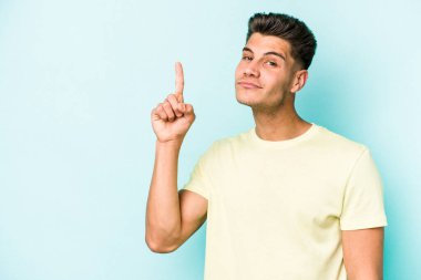 Mavi arka planda izole edilmiş genç beyaz adam bir numarayı parmağıyla gösteriyor..