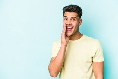 Mavi arka planda izole edilmiş genç beyaz adam yüksek sesle bağırıyor, gözleri açık ve elleri gergin tutuyor..