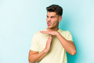 Mavi arka planda izole edilmiş genç beyaz bir adam bir mola hareketi gösteriyor..