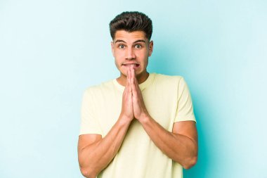 Mavi arka planda izole edilmiş genç beyaz bir adam el ele tutuşup, ağzının kenarında dua ediyor, kendinden emin..
