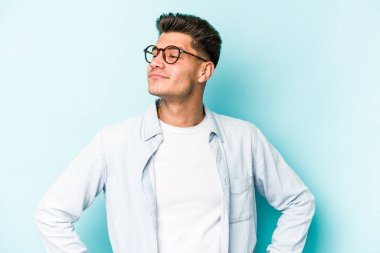 Kafkasyalı genç adam mavi arka planda izole edilmiş hedeflerine ve amaçlarına ulaşma hayali kuruyor.