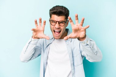 Mavi arka planda izole edilmiş genç beyaz adam gergin elleriyle çığlık atıyor..