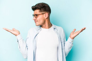 Kafkasyalı genç adam mavi arka planda izole edilmiş. Kafası karışmış ve omuz silkiyor. Kopya alanını tutmak için..