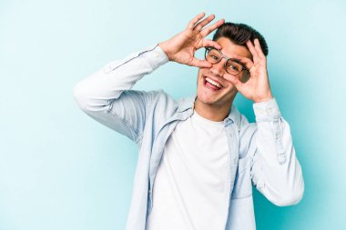 Mavi arka planda izole edilmiş genç beyaz adam gözlerinde sorun olmadığını gösteriyor.