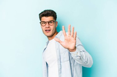 Mavi arka planda izole genç beyaz adam yakın bir tehlike nedeniyle şoka uğruyor