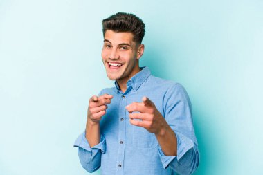 Mavi arka planda izole edilmiş genç beyaz adam parmaklarıyla ön tarafı işaret ediyor..