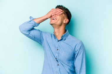 Mavi arka planda izole edilmiş genç beyaz adam ellerini başının üstünde tutarak neşe içinde gülüyor. Mutluluk kavramı.