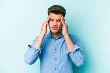 Genç beyaz adam mavi arka planda izole edilmiş tapınaklara dokunuyor ve başı ağrıyor..