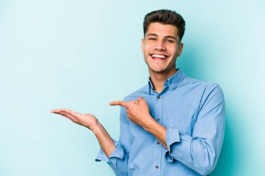 Kafkasyalı genç adam mavi arka planda izole edilmiş. Elinde palmiye ağacının bir kopyası olduğu için heyecanlı..