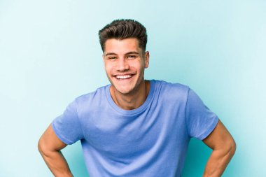 Mavi arka planda izole edilmiş genç beyaz adam mutlu, güler yüzlü ve neşeli.
