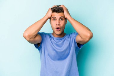 Kafkasyalı genç adam mavi arka planda izole edildi. Şaşırdı ve şok oldu..