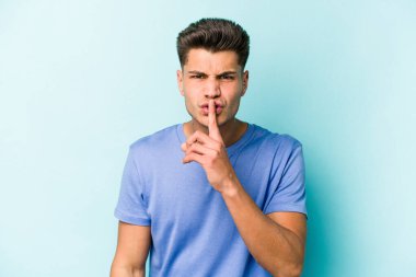 Mavi arka planda izole edilmiş genç beyaz bir adam ya sır saklıyor ya da sessizlik istiyor..