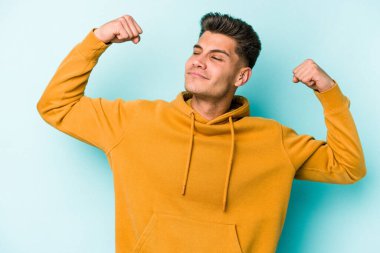 Mavi arka planda izole edilmiş genç beyaz adam güçlü bir hareket sergiliyor kollarıyla, kadınsı gücün sembolü.