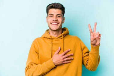 Kafkasyalı genç adam mavi arka planda izole edilmiş yemin ediyor, elini göğsüne koyuyor..