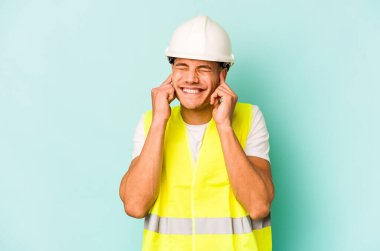 Kafkasyalı genç işçi mavi arka planda izole edilmiş kulakları elleriyle kapatıyor..