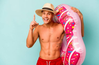 Mavi arka planda izole edilmiş şişme donut tutan genç beyaz bir adam bir fikri, ilham verici bir konsepti var..