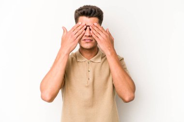 Beyaz arka planda izole edilmiş genç beyaz bir adam elleriyle gözlerini kapatmaktan korkuyor..