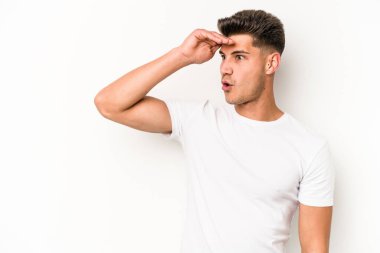 Beyaz arka planda izole edilmiş genç beyaz bir adam uzaklara bakıyor ve elini alnına koyuyor..