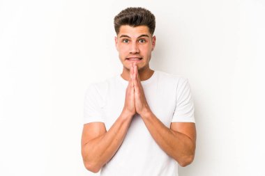 Beyaz arka planda izole edilmiş genç beyaz bir adam el ele tutuşup, ağız kenarında dua ediyor, kendinden emin..