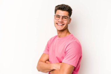 Beyaz arka planda kendini güvende hisseden, kararlılıkla kollarını kavuşturan beyaz tenli genç bir adam..