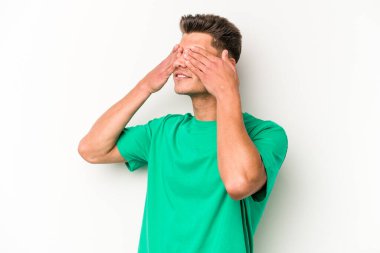 Beyaz arka planda izole edilmiş genç beyaz bir adam elleriyle gözlerini kapatmaktan korkuyor..
