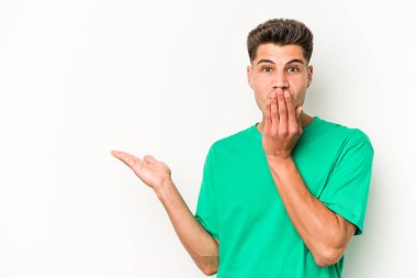 Beyaz arka planda izole edilmiş genç beyaz adam, avuç içi fotokopi alanını elinde tutmaktan etkilenmiş..