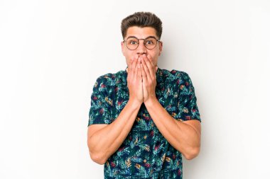 Beyaz arka planda izole edilmiş genç beyaz adam elleriyle ağzını kapatırken şok oldu..