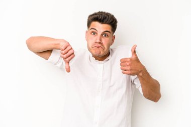 Beyaz arka planda izole edilmiş genç beyaz bir adam baş parmaklarını aşağı ve yukarı kaldırıyor, zor seçim konsepti