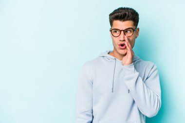 Mavi arka planda izole edilmiş genç beyaz bir adam gizli bir sıcak fren haberi veriyor ve yana bakıyor.