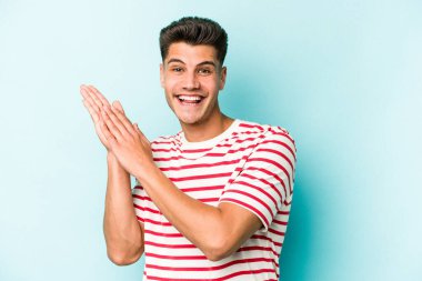 Kafkasyalı genç adam mavi arka planda izole edilmiş enerjik ve rahat hissediyor, ellerini ovuşturuyor kendinden emin.