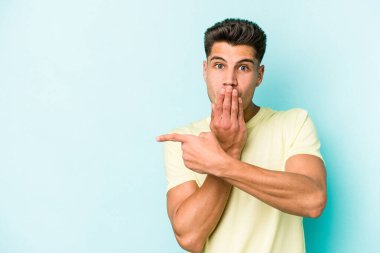 Mavi arka planda izole edilmiş genç beyaz adam yan tarafı işaret ediyor.