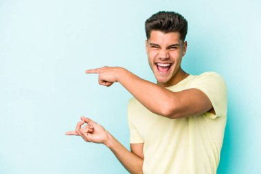 Kafkasyalı genç adam mavi arka planda izole edilmiş. İşaret parmağıyla işaret ettiği için heyecanlı..