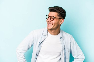 Kafkasyalı genç, mavi arka planda izole edilmiş. Kendine güvenen, kalçaları tutan biri..