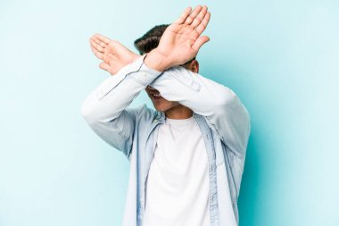 Kafkasyalı genç adam mavi arka planda izole edilmiş iki kolu çapraz tutuyor, inkar kavramı.