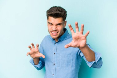 Mavi arka planda izole edilmiş genç beyaz adam pençelerini kedi taklidi yaparken gösteriyor, agresif bir hareket..