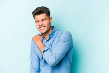 Mavi arka planda izole edilmiş, omuz ağrısı olan genç beyaz bir adam..