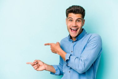 Kafkasyalı genç adam mavi arka planda izole edilmiş. İşaret parmağıyla işaret ettiği için heyecanlı..