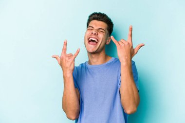 Mavi arka planda izole edilmiş genç beyaz adam boynuzlarını devrim konsepti olarak gösteriyor..