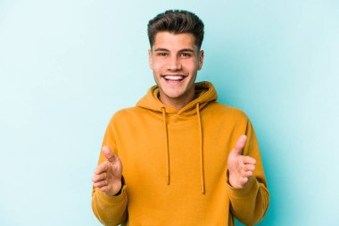 Mavi arka planda izole genç beyaz adam iki eliyle bir şey tutuyor, ürün sunumu..