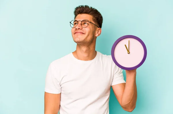 Young Caucasian Man Holding Clock Isolated Blue Background Dreaming Achieving — Stock Fotó