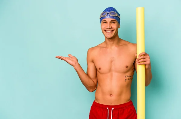 年轻的高加索游泳运动员 手握泡沫棒 蓝色背景隔离 手掌上有一个复制空间 腰部有另一只手 — 图库照片